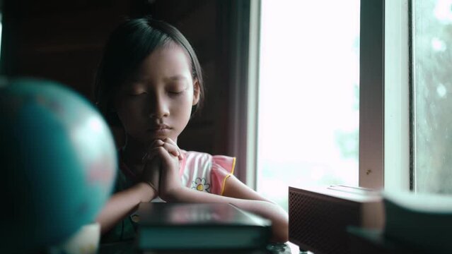Child girl praying on bible with light in morning at home, christian concept. High quality 4k video.