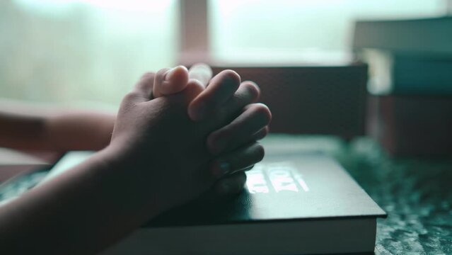 Hands of child girl praying on table with light in morning at home, christian concept. High quality 4k video.