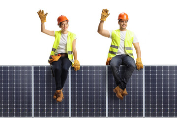 Male and female construction workers sitting on a solar panel and waving