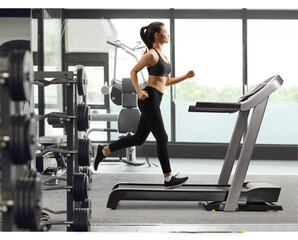 Fototapeta na wymiar Young female in black leggings running on a treadmill at a gym