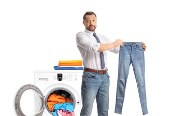 Man standing in front of a washing machine and holding a small pair of jeans