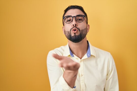 Hispanic young man wearing business clothes and glasses looking at the camera blowing a kiss with hand on air being lovely and sexy. love expression.