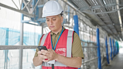 Young caucasian man architect using smartphone at construction place