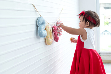 Cute little girl in red dress interested with numbers hanging on string are made of fabric, hanging...