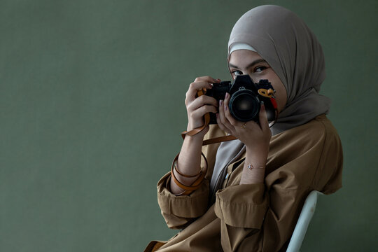 Pretty Muslim girl in hijab holding vintage camera over background in studio, taking camera