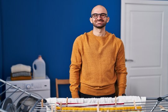 Young bald man with beard hanging clothes at clothesline with a happy and cool smile on face. lucky person.