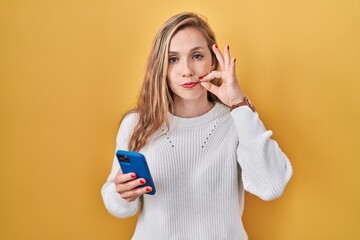Young blonde woman using smartphone typing message mouth and lips shut as zip with fingers. secret and silent, taboo talking © Krakenimages.com