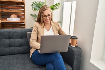 Naklejka premium Young blonde woman psychologist using laptop drinking coffee at psychology clinic