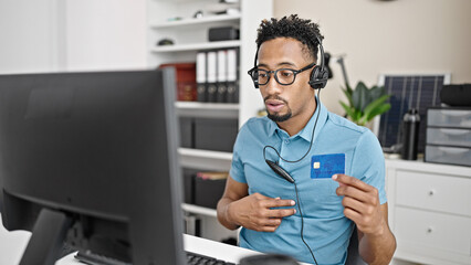 African american man business worker wearing headset on a video call using credit card at office
