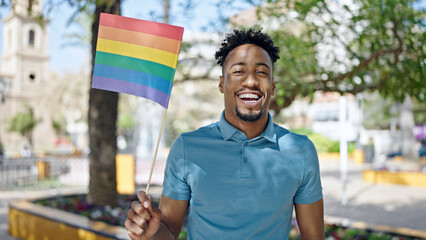 African american man smiling confident holding rainbow flag at park