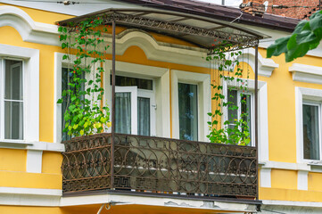 Balcony on an old 19th century house with climbing plants. The facade of the balcony with metal decorations.