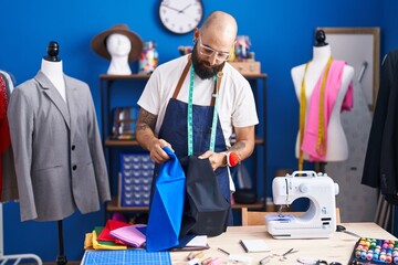 Young bald man tailor holding cloths at clothing factory