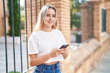 Fototapeta premium Young blonde woman smiling confident using smartphone at street