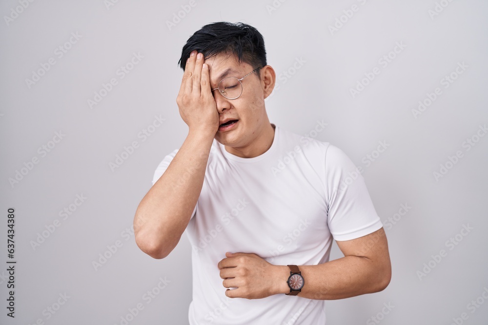 Sticker Young asian man standing over white background yawning tired covering half face, eye and mouth with hand. face hurts in pain.