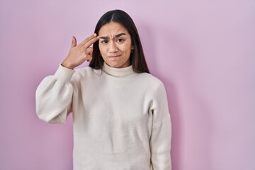 Young south asian woman standing over pink background shooting and killing oneself pointing hand and fingers to head like gun, suicide gesture.