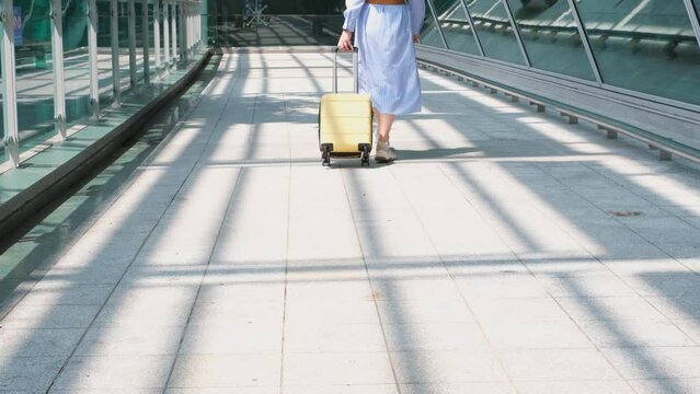 Young woman rolls yellow suitcase near the airport, back view.