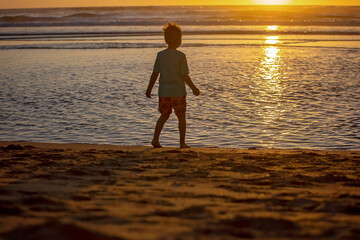 Happy children, boys, playing on the beach on sunset, kid cover in sand, smiling, laughing