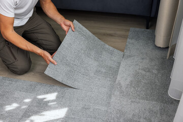 man installing self adhesive carpet tiles on floor in living room at home - 637437988
