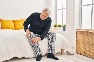 Fotobehang Lengtemeter Senior man suffering for knee pain sitting on bed at bedroom