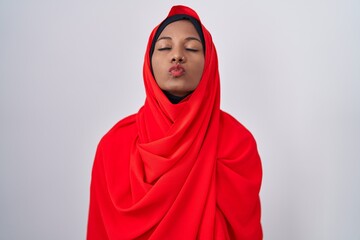 Young arab woman wearing traditional islamic hijab scarf looking at the camera blowing a kiss on air being lovely and sexy. love expression.