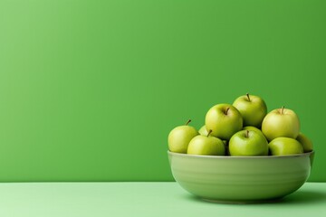 Green apples in bowl on green background.