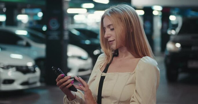 female stands in parking lot, engrossed in latest news use mobile application. soft glow of screen casts faint reflection on her face, she is focused use mobile application.