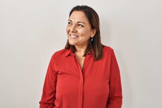 Hispanic mature woman standing over white background looking away to side with smile on face, natural expression. laughing confident.