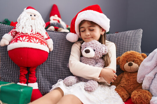 Adorable hispanic girl hugging teddy bear sitting on sofa by christmas decoration at home