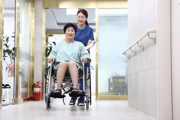 Fototapeta na wymiar 병원의 복도에서 간호사가 휠체어 탄 환자와 마주보며 격려하는 모습