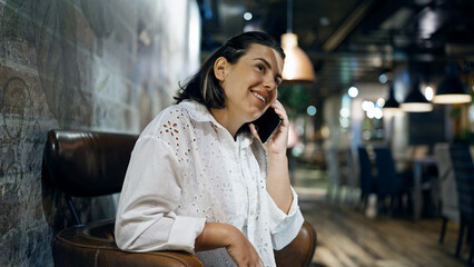 Fototapeta na wymiar Beautiful young hispanic woman talking on smartphone smiling at cafeteria