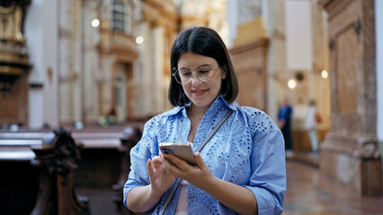 Young beautiful hispanic woman visiting church using smartphone standing at St. Karl BorromÃ¤us...