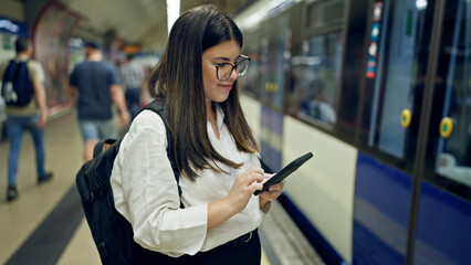 Young beautiful hispanic woman waiting for the subway using smartphone in subway station of Madrid