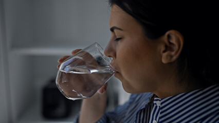 Young beautiful hispanic woman drinking a glass of water at the kitchen