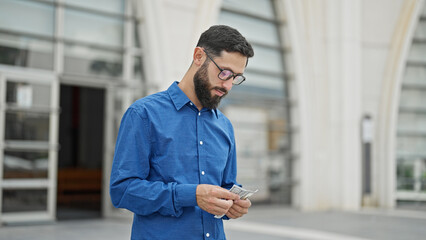 Young hispanic man business worker standing with serious face counting dollars at street