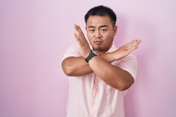 Chinese young man standing over pink background rejection expression crossing arms doing negative sign, angry face