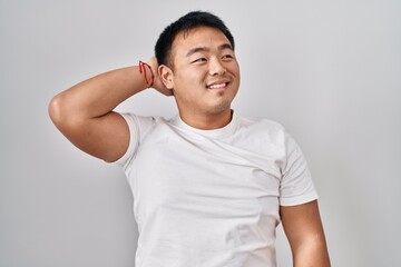 Young chinese man standing over white background smiling confident touching hair with hand up gesture, posing attractive and fashionable