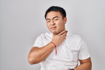 Young chinese man standing over white background touching painful neck, sore throat for flu, clod and infection