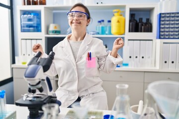 Fototapeta premium Hispanic girl with down syndrome working at scientist laboratory celebrating surprised and amazed for success with arms raised and eyes closed. winner concept.