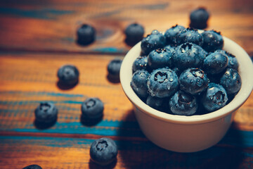 Freshly picked juicy blueberries in the bowl on wooden background, close up
