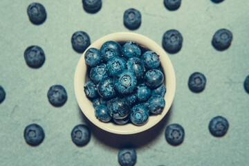Freshly picked juicy blueberries in the bowl on blue background, close up