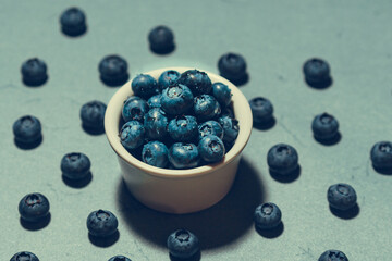 Freshly picked juicy blueberries in the bowl on blue background, close up