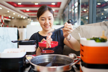 Happy - cheerful Asian fat woman enjoy eating a traditional Asian Hotpot or Sukiyaki in the Asian...