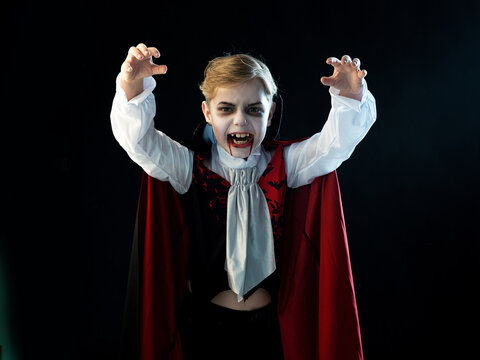 Portrait of boy wearing Halloween vampire makeup and costume cloak bared his teeth, isolated on black background