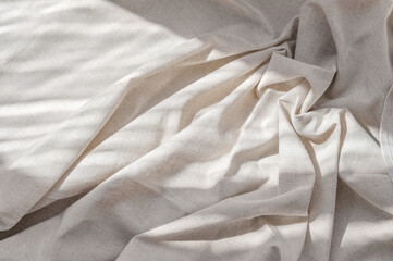 Crumpled neutral beige linen fabric texture with folds and natural lifestyle sunlight shadows,...