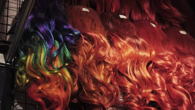 Showcase of natural colorful wigs in different colors fixed on the metal wig holders in beauty salon. Asian comic shop.