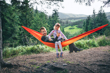happy father with daughter on hammock mountains on background