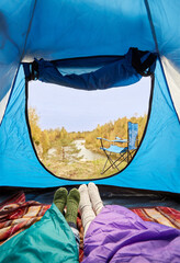 travel, tourism and camping concept - view to river from camp tent with feet in warm socks under sleeping bags