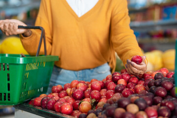 Detail of a customer's hands picking plums at a neighborhood store.