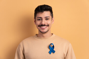 joyful caucasian man showing blue ribbon in all beige colors. prostate cancer, awareness concept.