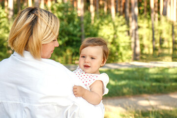 cute baby girl in the park in her mother's arms on a sunny summer day